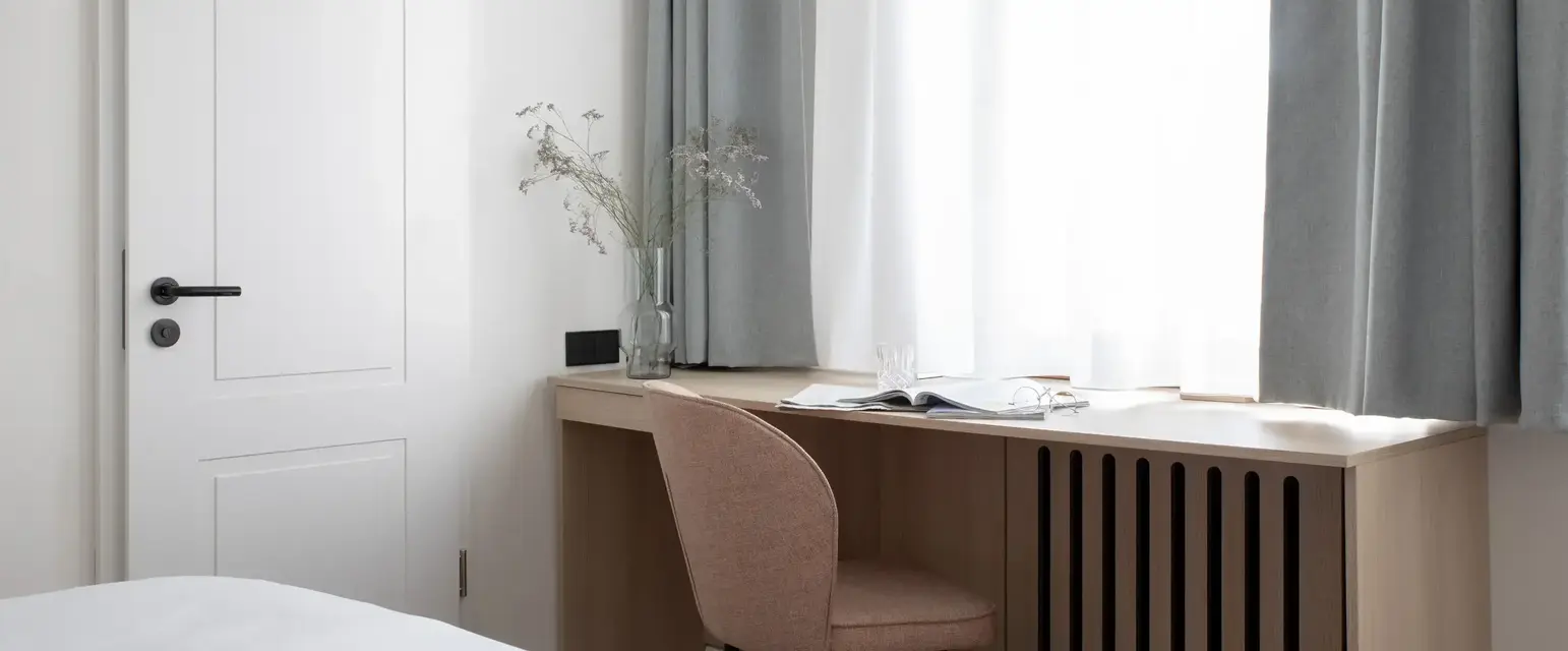 a desk with a chair and a vase of flowers in front of a window