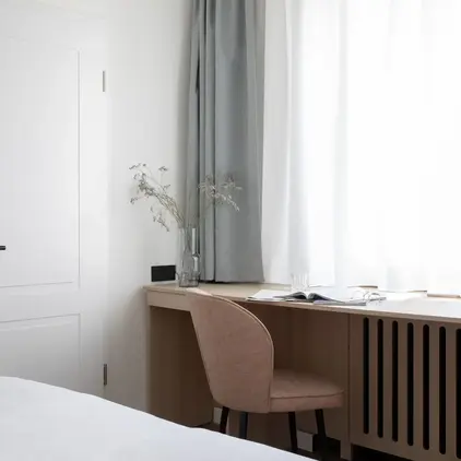 a desk with a chair and a vase of flowers in front of a window