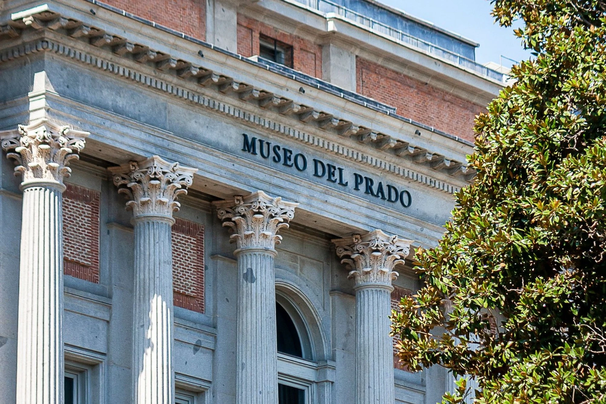 The columns and facade of the Museo del Prado under a blue sky.