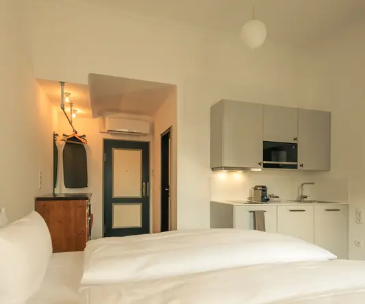 a room with white bedding and a kitchen