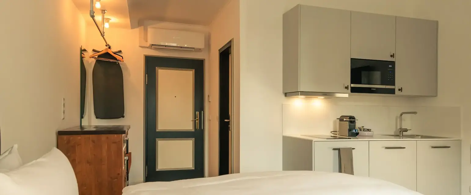 a room with white bedding and a kitchen