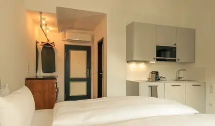 a room with white bedding and a kitchen