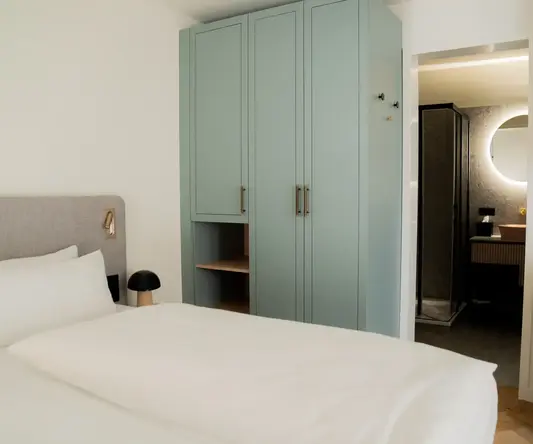 a bed with white sheets and a blue wardrobe