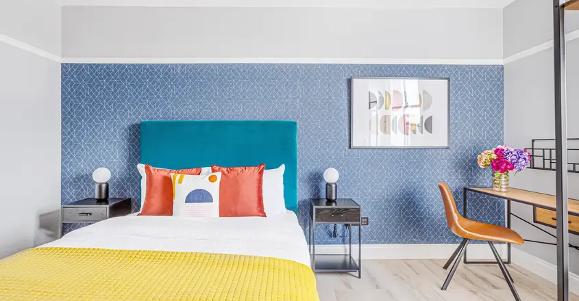 a bed with a yellow blanket and a blue wallpaper