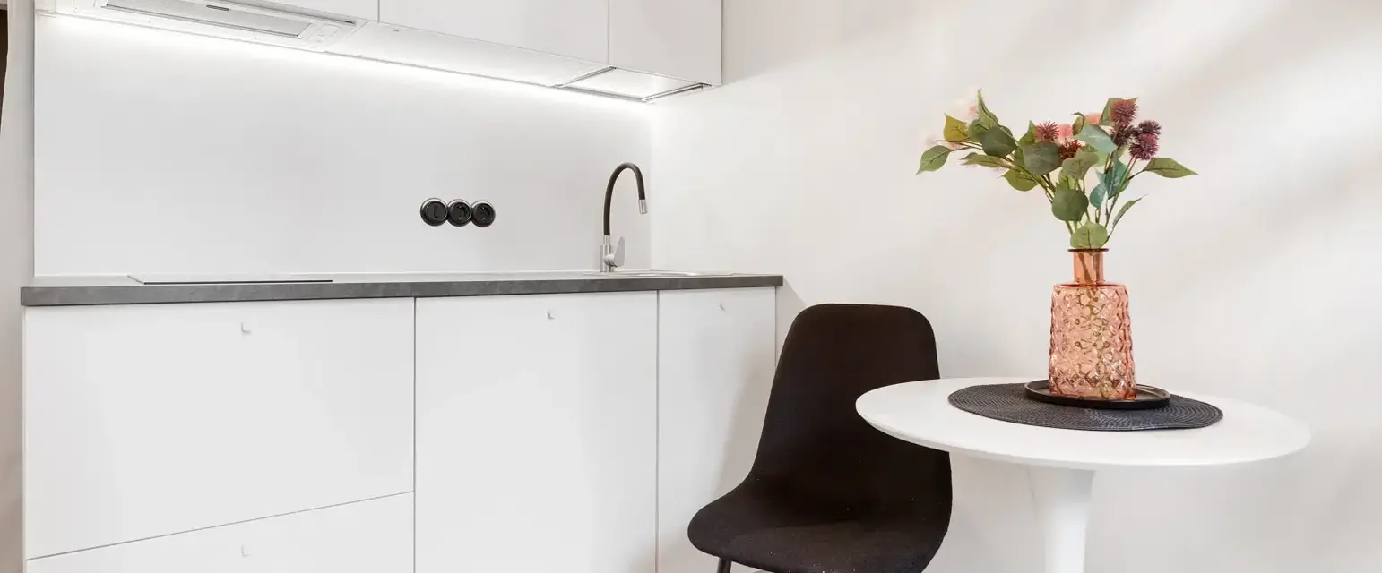 a white kitchen with a table and a vase of flowers