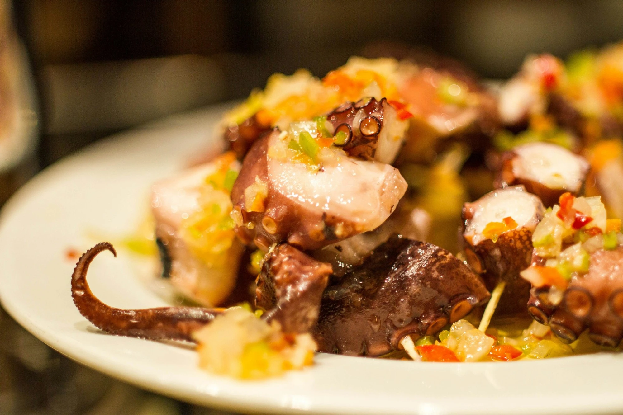 A plate of grilled octopus pieces on skewers, topped with chopped peppers and onion.