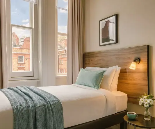 a bed with a lamp and a table in front of windows