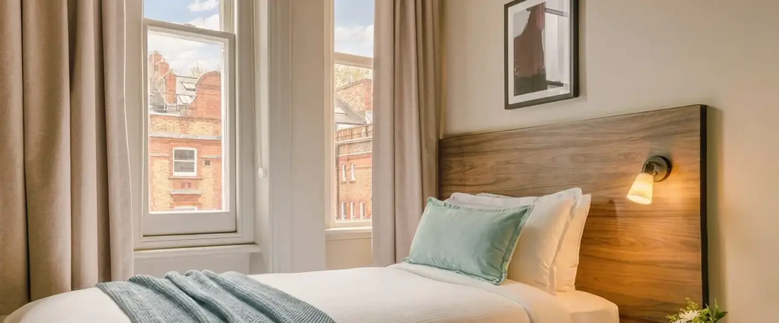 a bed with a lamp and a table in front of windows