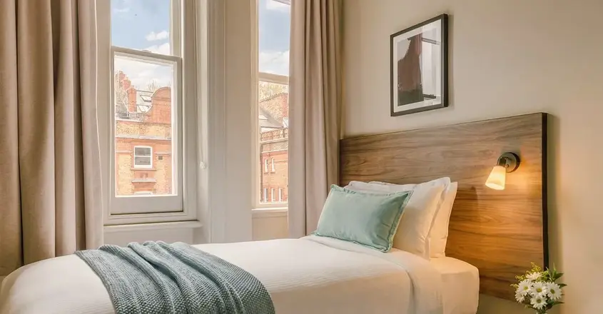 a bed with a lamp and a table in front of windows