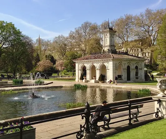 a man sitting on a bench in front of a pond with a fountain
