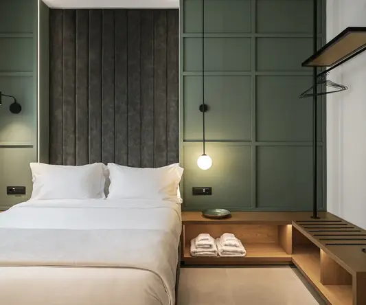 a bed with white sheets and a shelf with towels