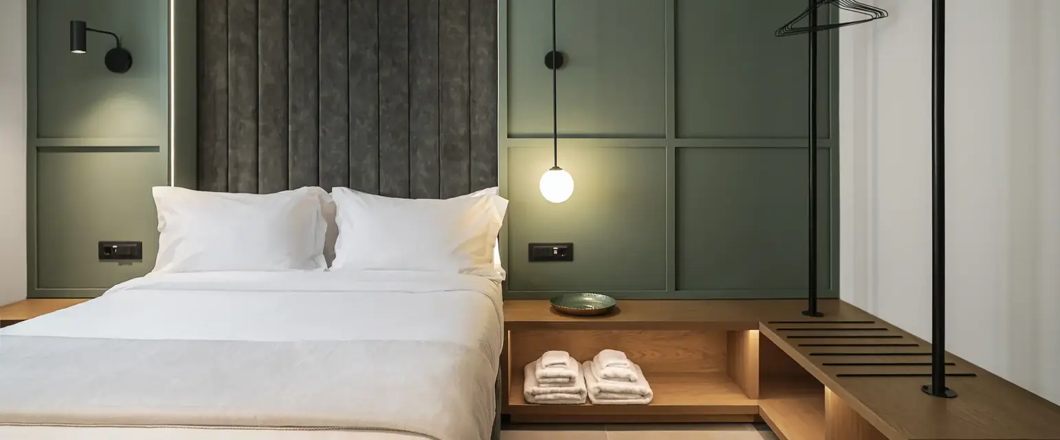 a bed with white sheets and a shelf with towels