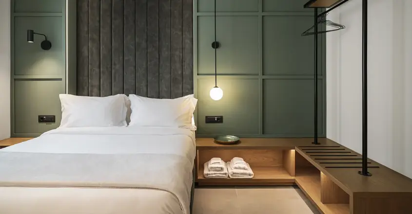a bed with white sheets and a shelf with towels