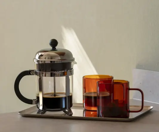 a coffee maker and two cups on a tray