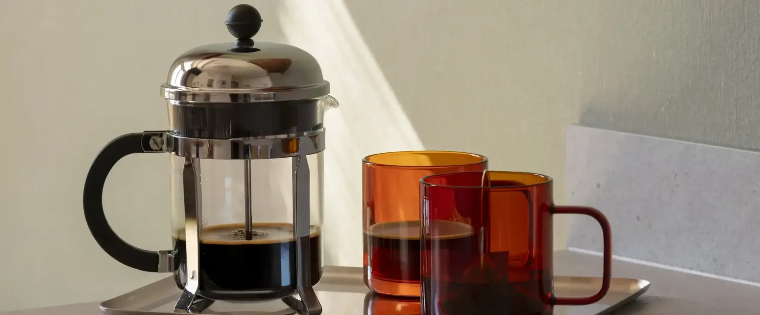 a coffee maker and two cups on a tray