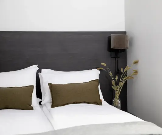 a bed with pillows and a vase of dry grass