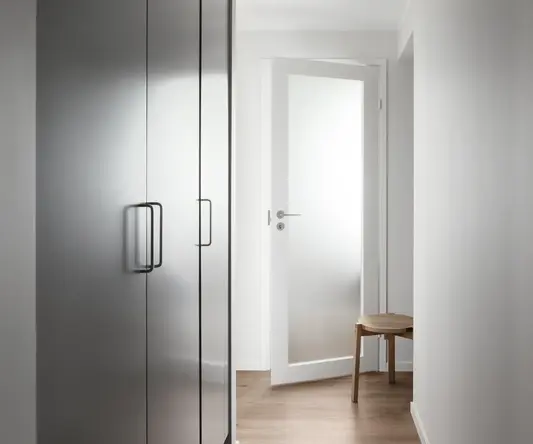a white hallway with a wooden stool and a door