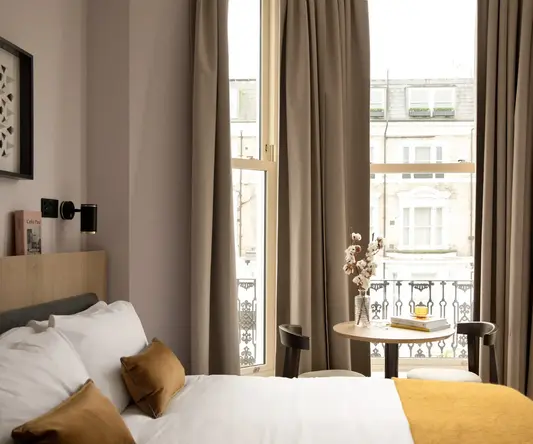 a bed with a table and a vase of flowers in front of a window