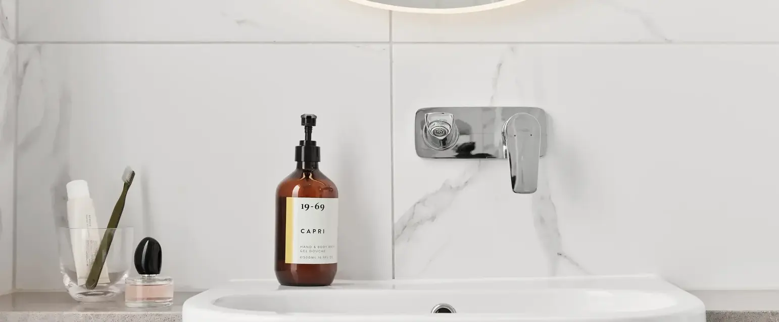 a white sink with a round mirror and a bottle of liquid on it