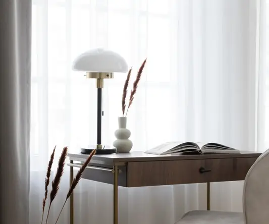 a desk with a lamp and a book in a room with curtains