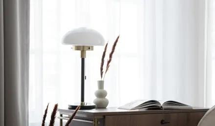 a desk with a lamp and a book in a room with curtains