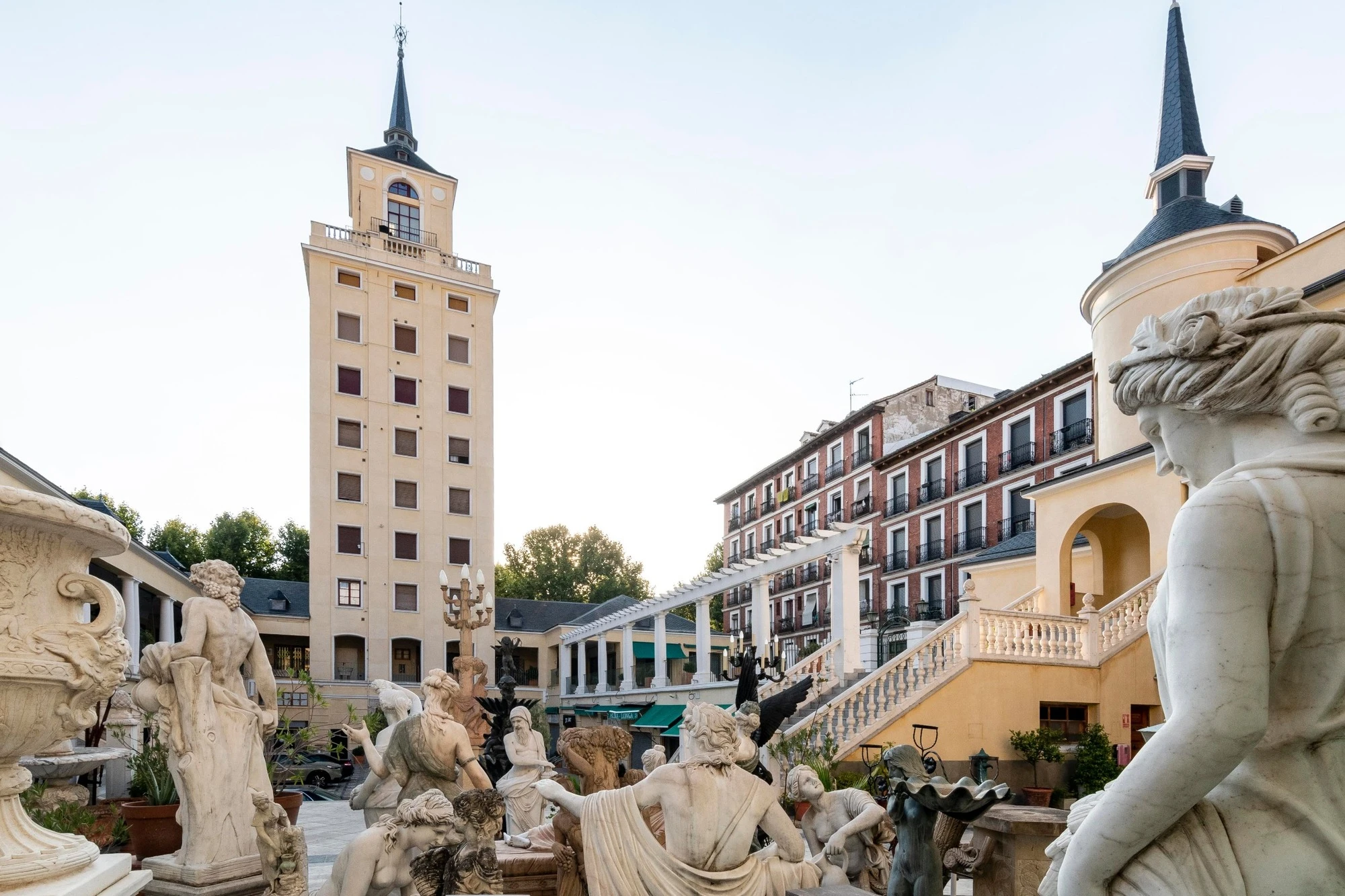 A courtyard with marble statues in front of a tall yellow tower.
