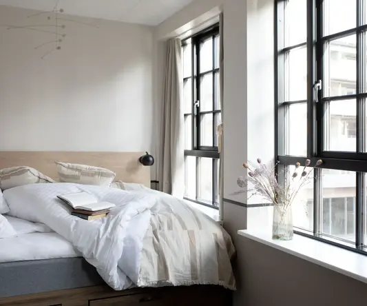 a bed with a book and a vase of flowers in a window