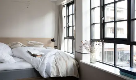 a bed with a book and a vase of flowers in a window