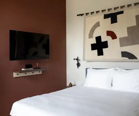 a bed with a white sheet and a black television above it