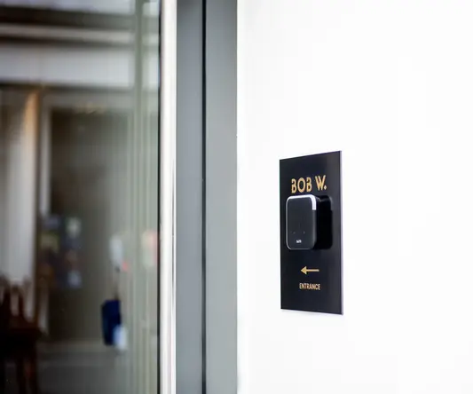 a black rectangular sign with a square black square on a white wall
