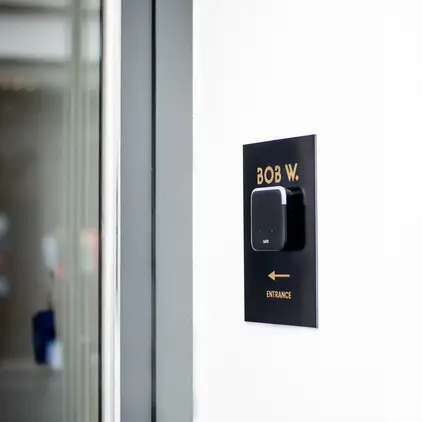 a black rectangular sign with a square black square on a white wall