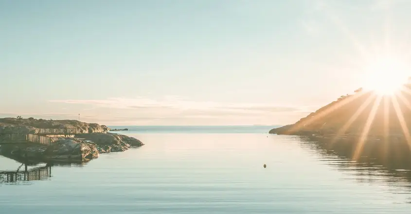 a body of water with rocks and a hill in the background