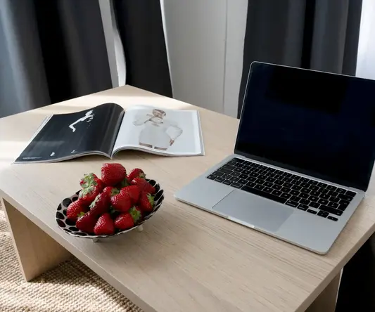 a laptop on a table with a bowl of strawberries