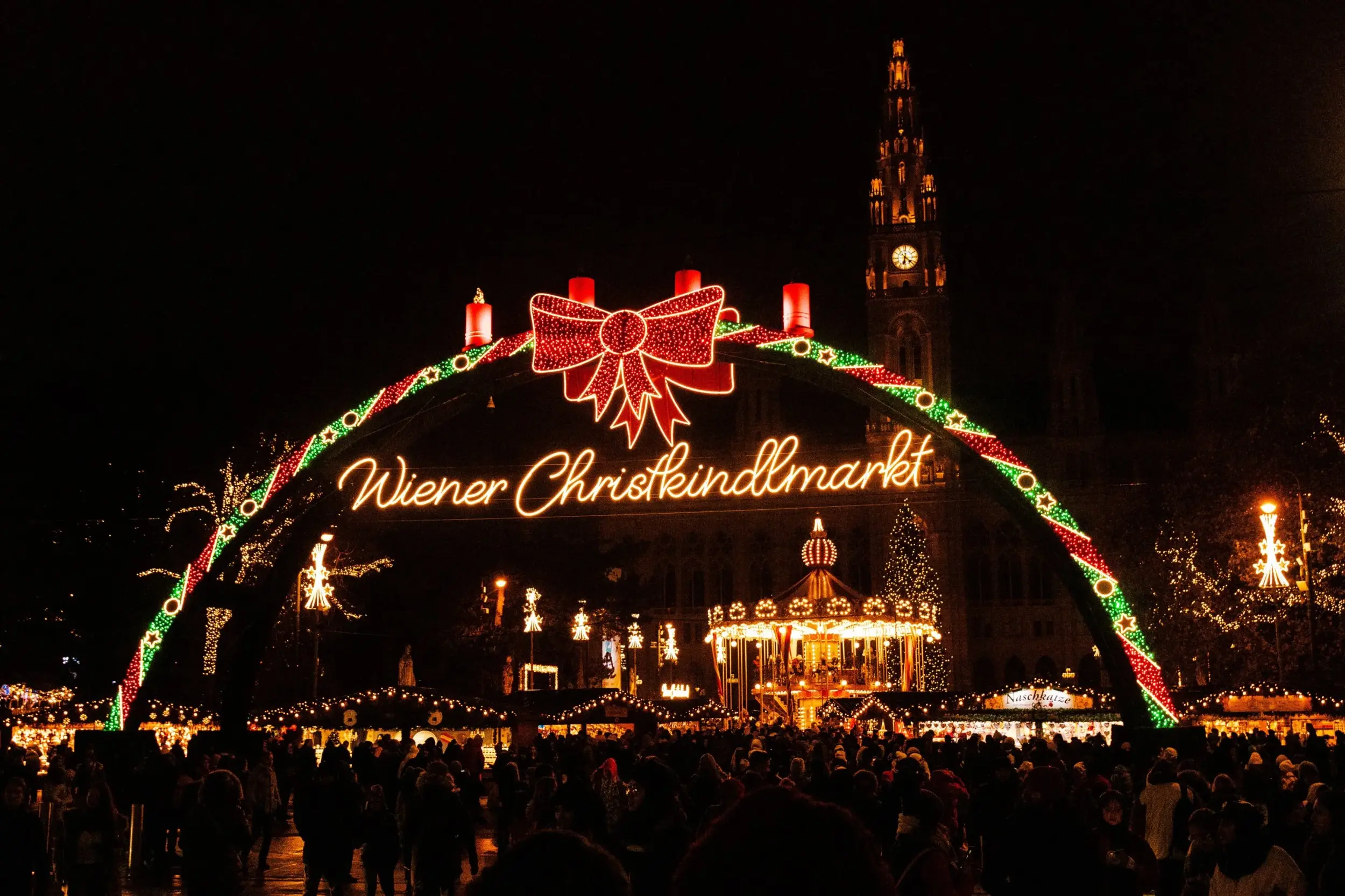 The lit Wiener Christkindlmarkt arch in front of Vienna City Hall at night