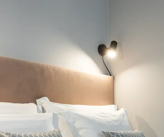 a bed with pillows and a light on the wall