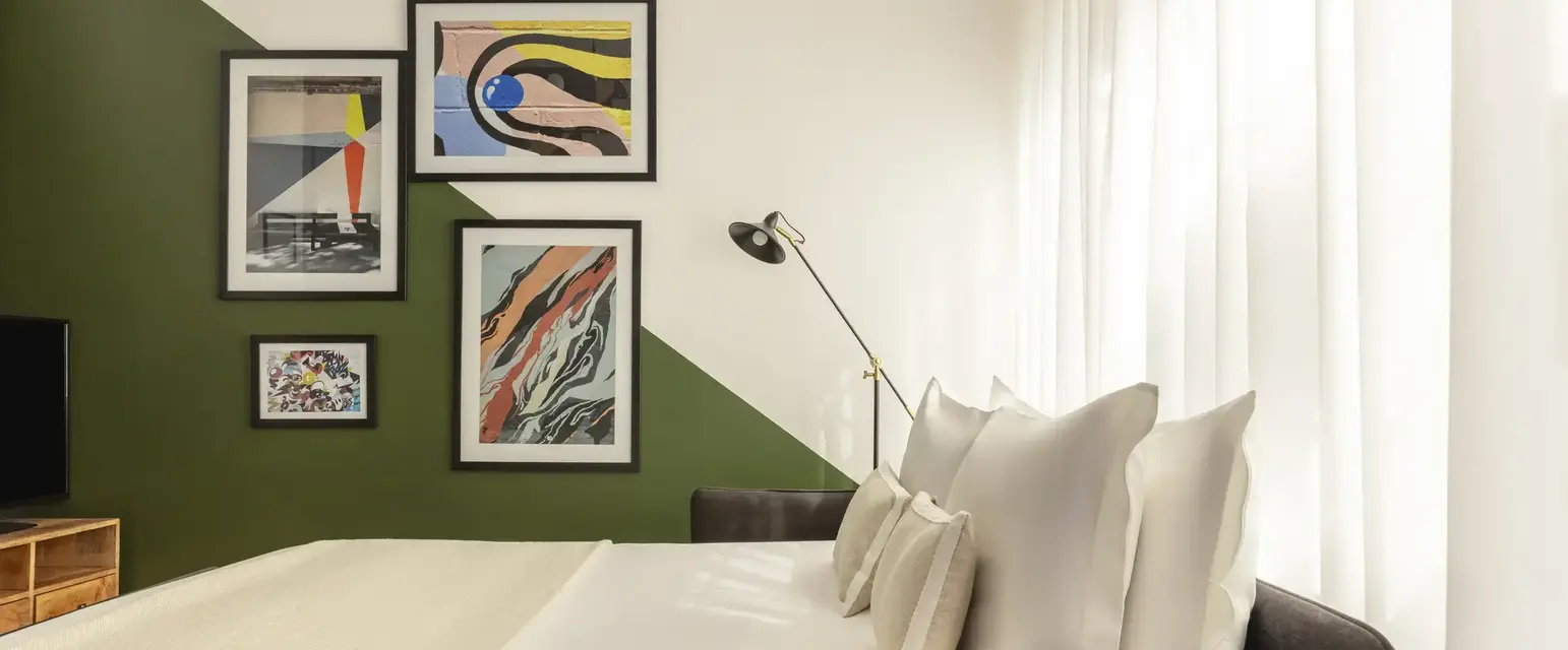 a bed with white pillows and a green wall with pictures on the wall